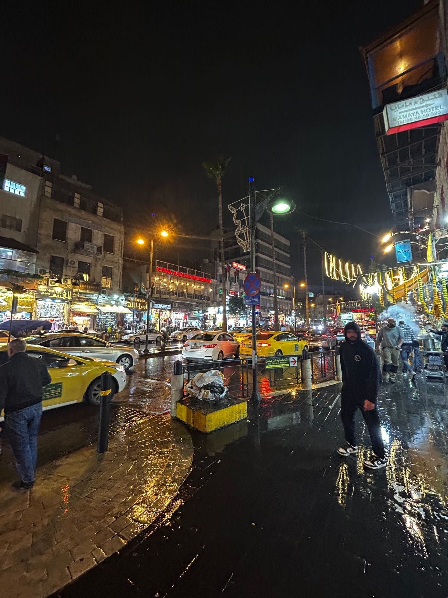 Amman street at night with Arabic labels floating over shops, a taxi, and the road